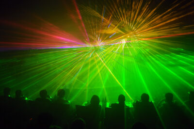 Row of people seated as audience members facing a green and yellow laser light show