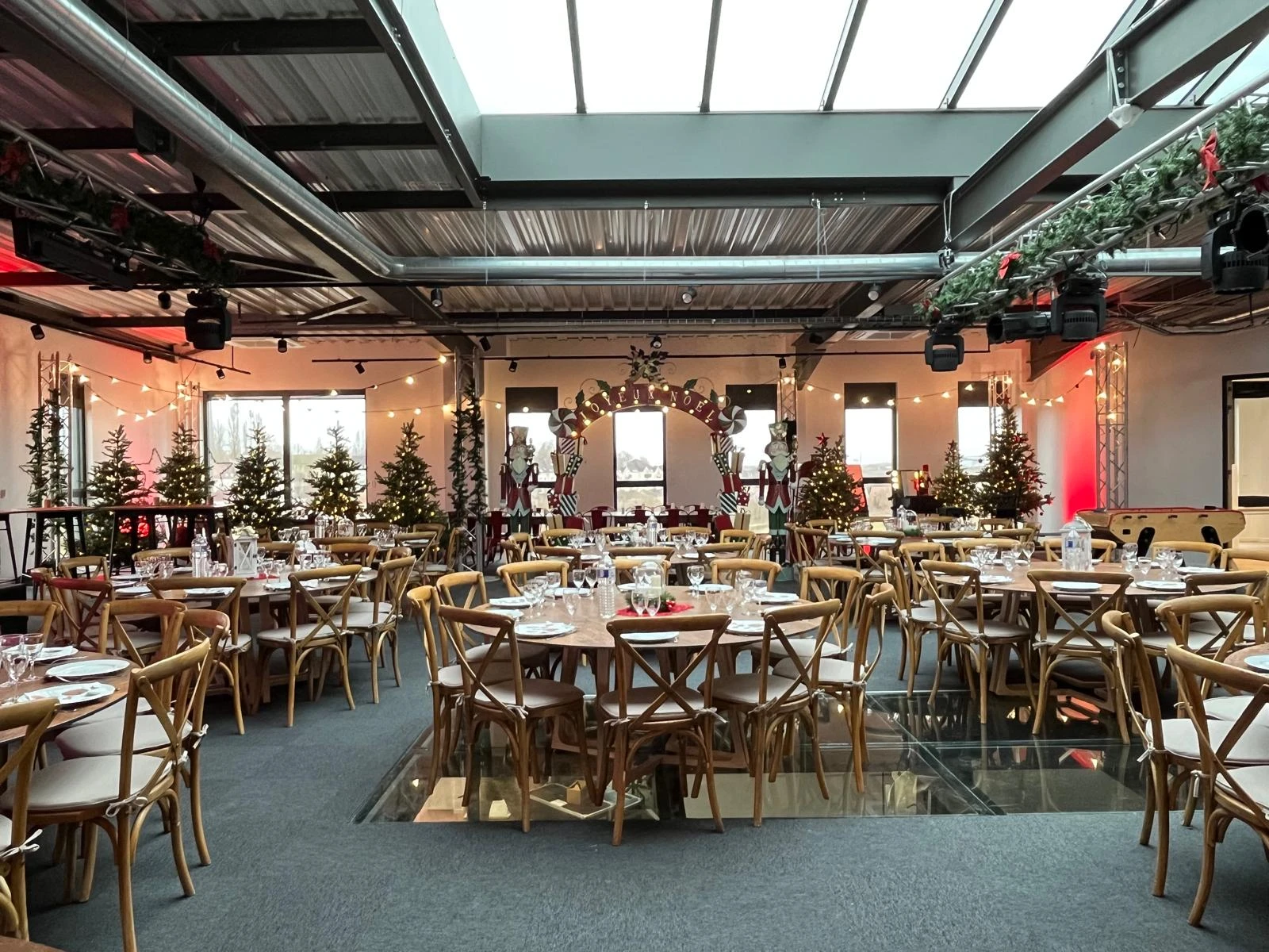 Salle de réception de Noël avec tables rondes, chaises bistrot en bois, sapins illuminés, guirlandes et arche encadrée de casse-noisettes géants